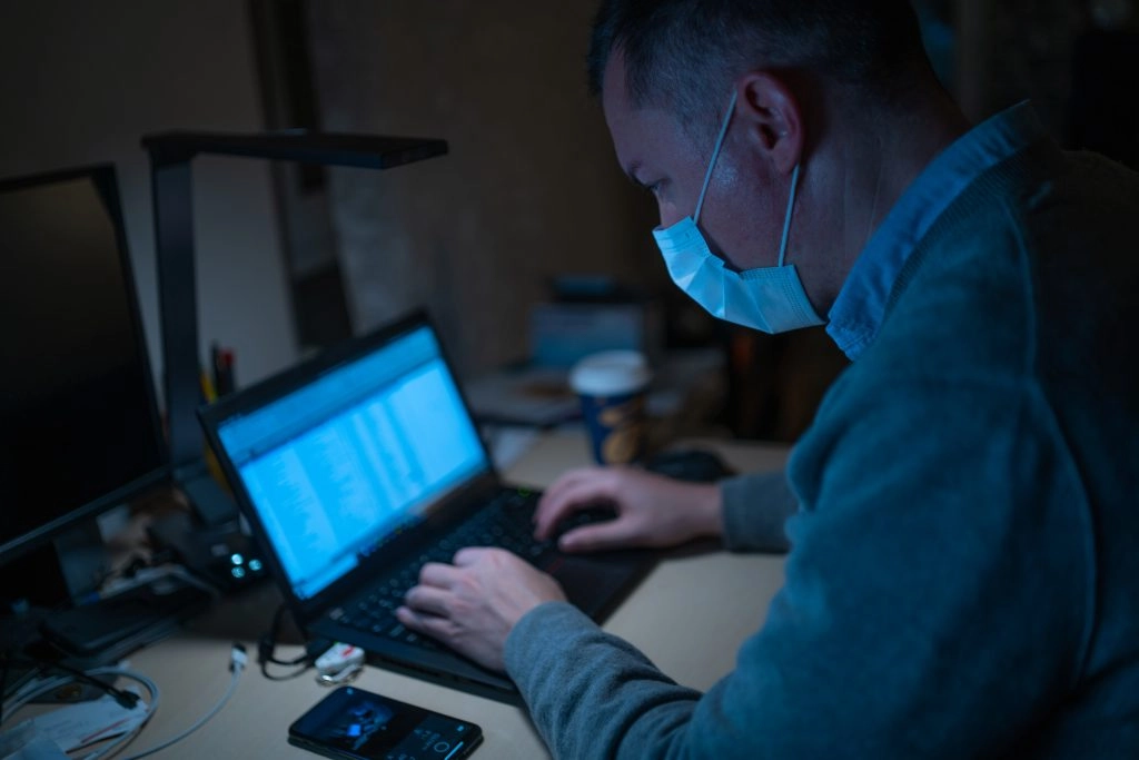 Man With Face Mask Types on Computer