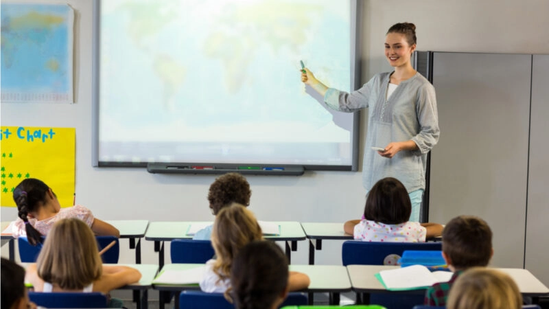Teacher stands in front of her classroom and points to a projection screen